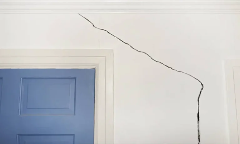 Large diagonal wall crack extending from the ceiling above a doorway, indicating possible structural movement or foundation settlement inside a residential property.